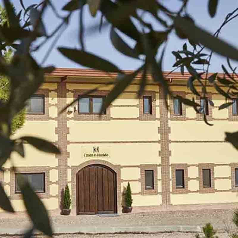 Blick auf das Firmengebäude von Casas de Hualdo, umgeben von Olivenzweigen in Spanien.