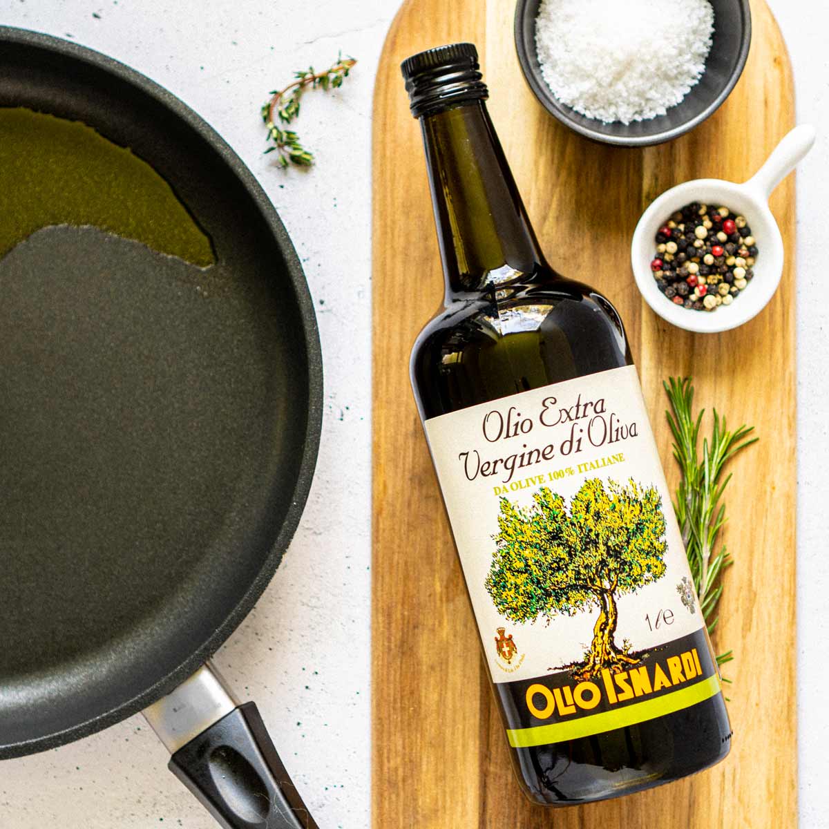 Olio Isnardi Olivenöl neben Pfanne, Gewürzen und Kräutern.