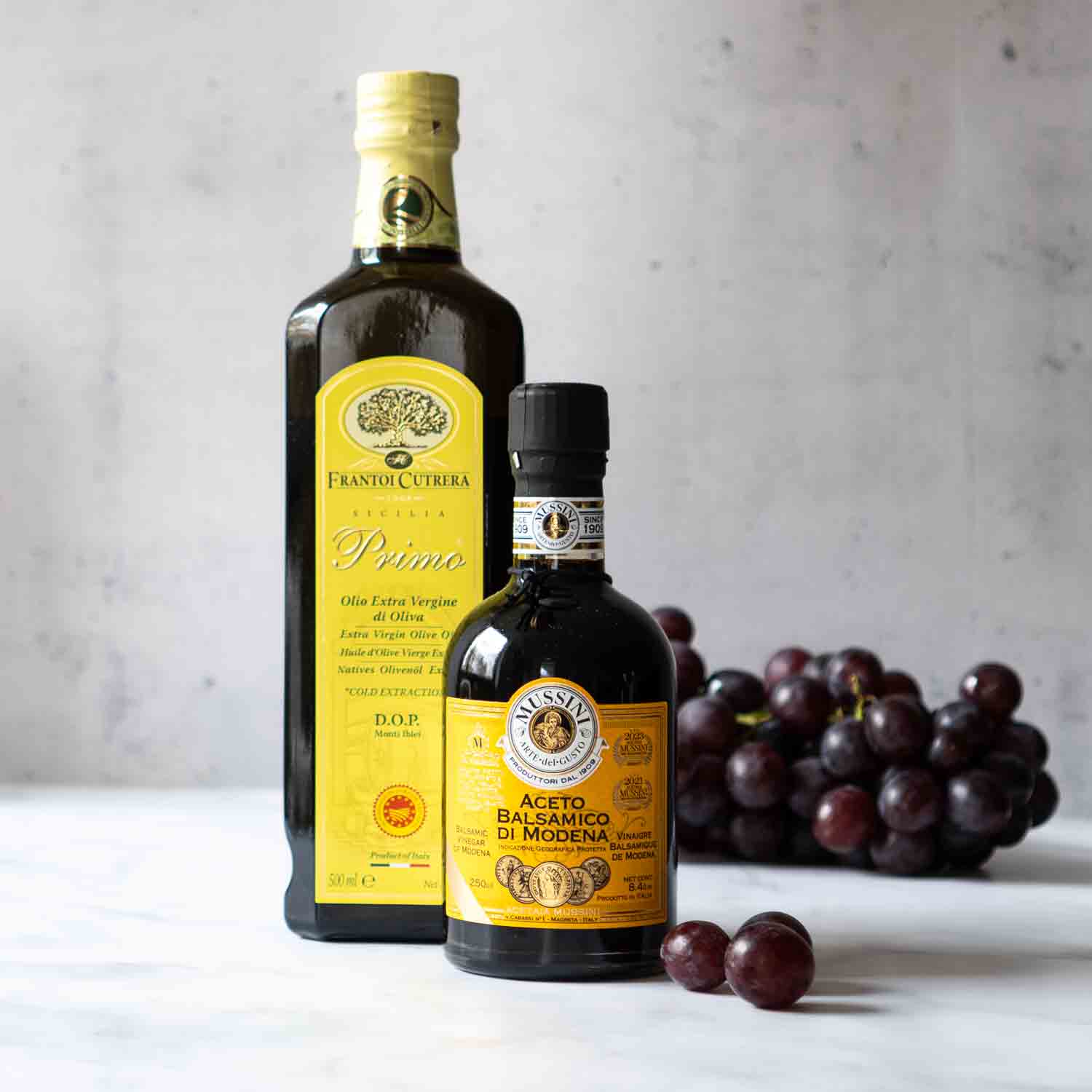 Olivenöl und Balsamico-Essig mit Trauben im Hintergrund.