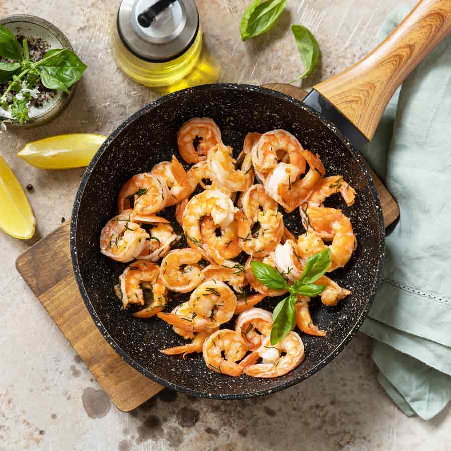 Garnelen in Pfanne mit Olivenöl und Basilikumblättern.