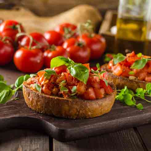 Bruschetta mit Tomaten und Basilikum auf Holzbrett serviert.