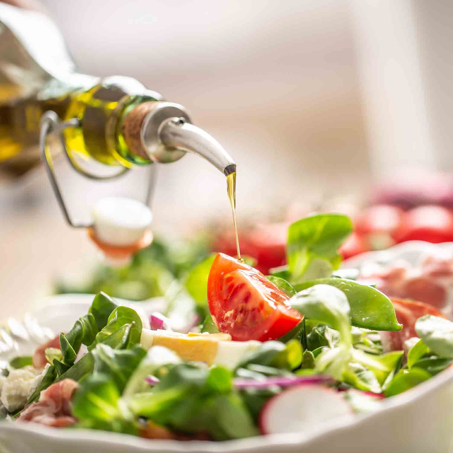 Olivenöl wird über frischen Salat mit Tomaten gegossen.