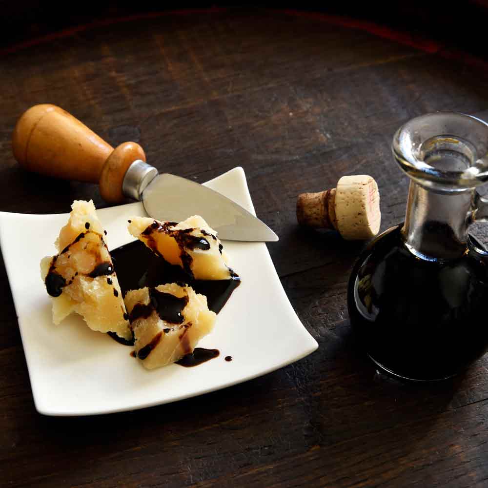 Parmesan mit Balsamico, Messer und Flasche auf Tisch.