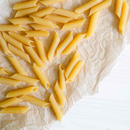 Penne Rigate Nudeln auf Pergamentpapier verstreut.