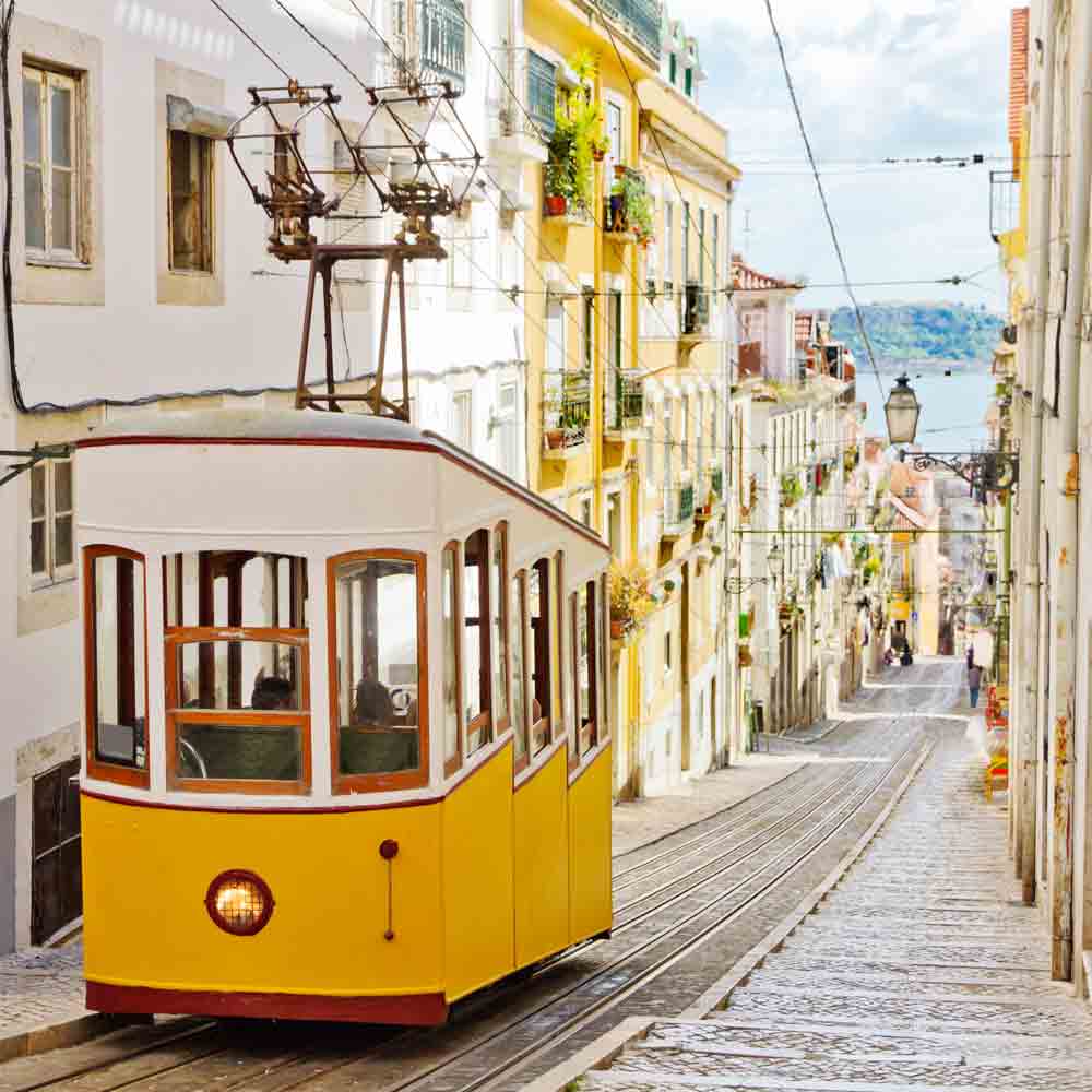 Gelbe Straßenbahn fährt in Lissabon in einer engen Gasse die Straße hinunter