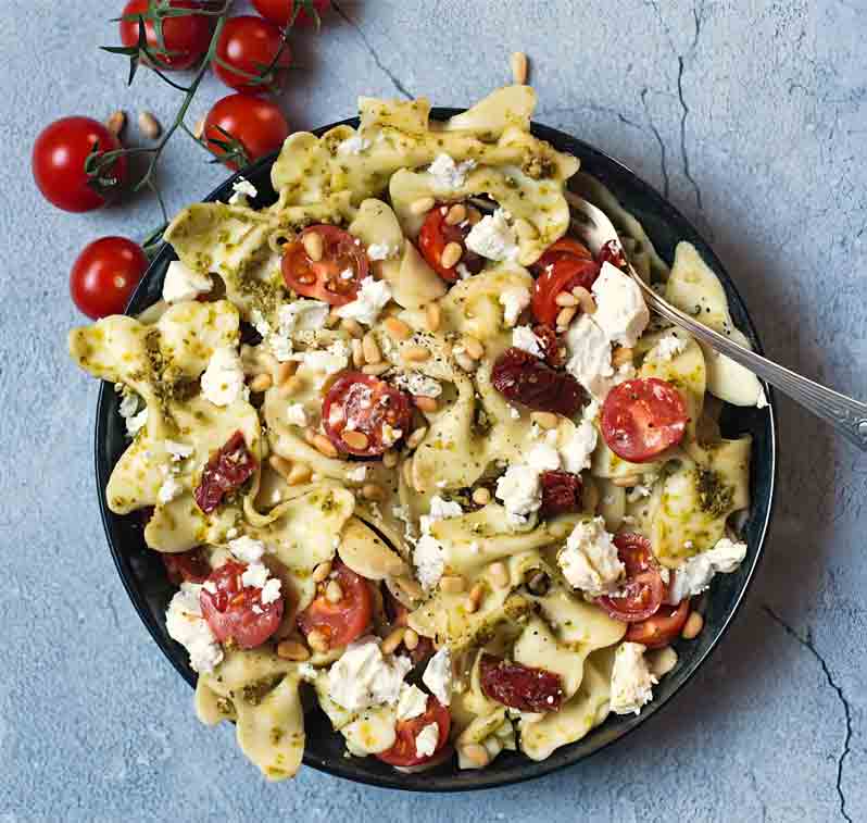 Pasta mit Pesto, Tomaten, Pinienkernen und Käse auf Teller.