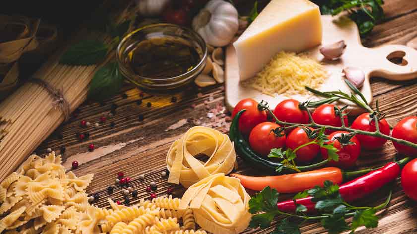 Pasta, Tomaten, Olivenöl, Käse, Kräuter, Knoblauch, Peperoni, Holzbrett.