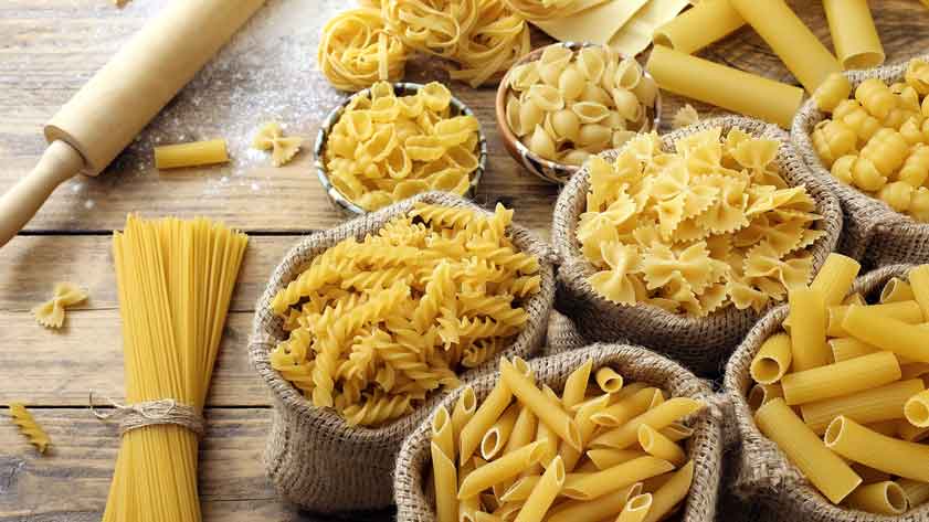 Verschiedene Nudelsorten in Jutesäcken auf Holztisch.