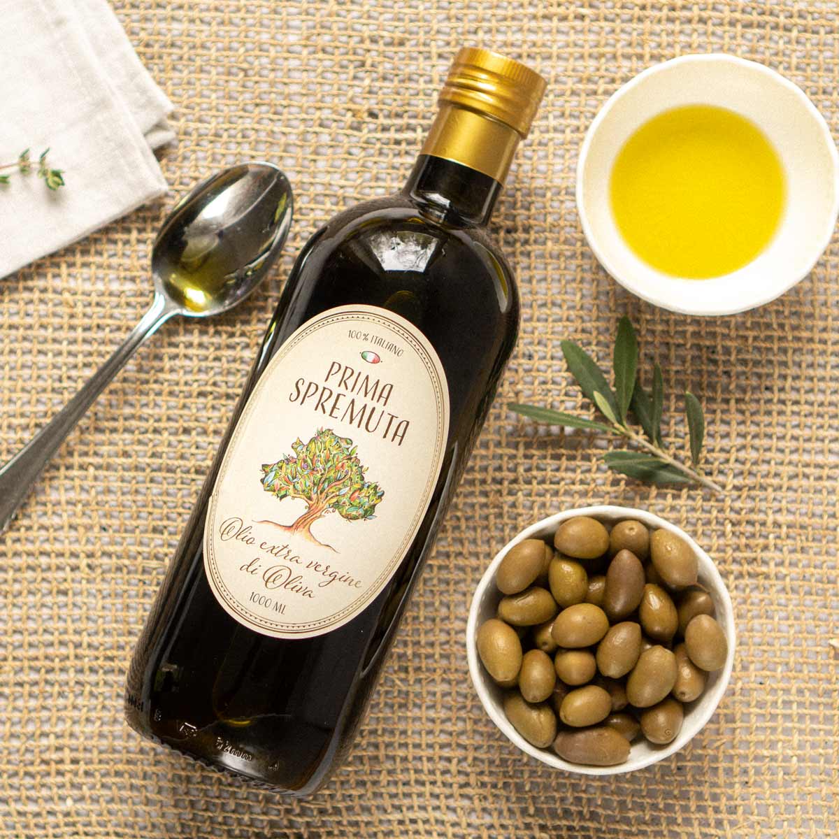 Olivenölflasche Prima Spremuta, Schale mit Oliven, Löffel.
