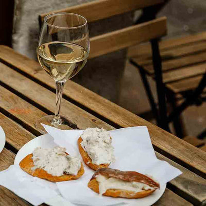 Weinglas und Crostini auf Holztisch im Freien.