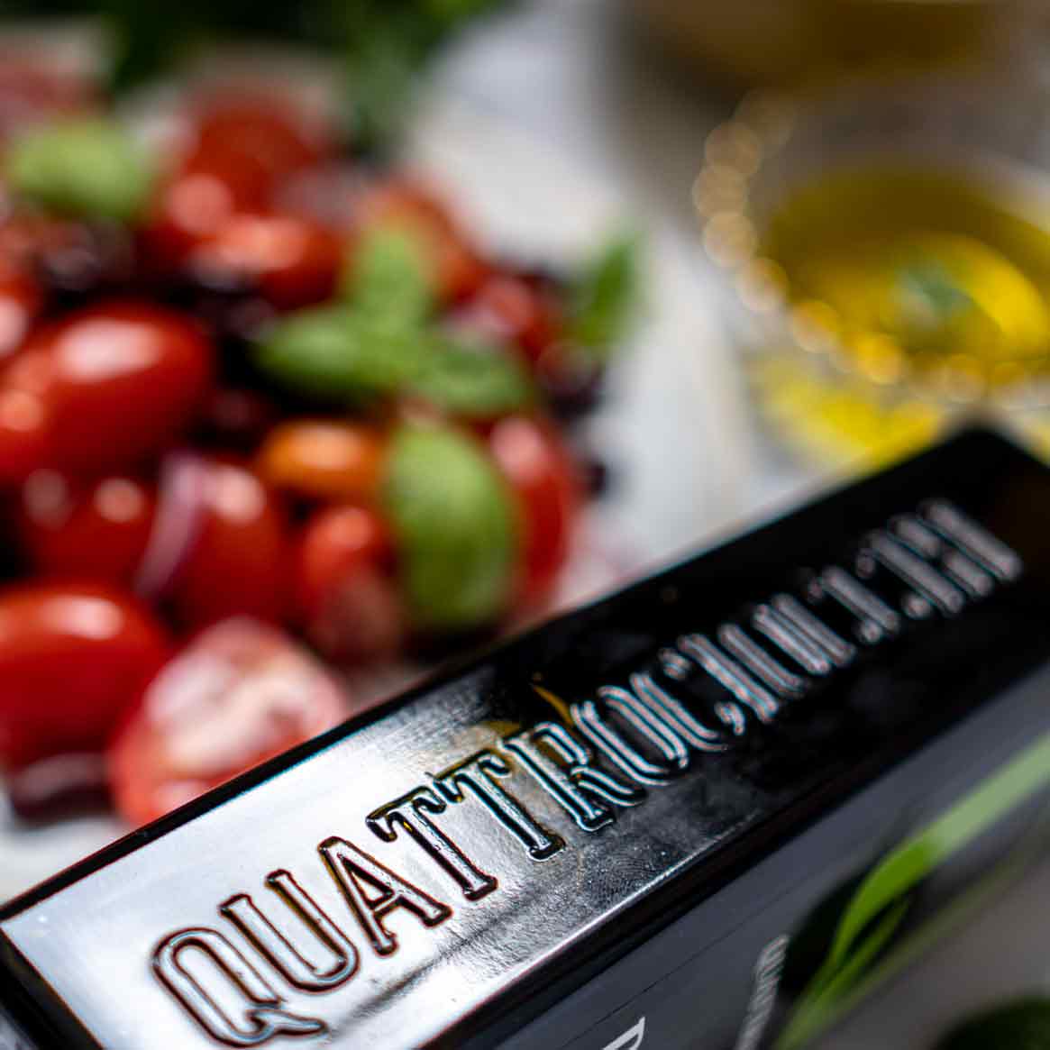 Quattrociocchi Olivenöl neben Tomaten und Basilikum.
