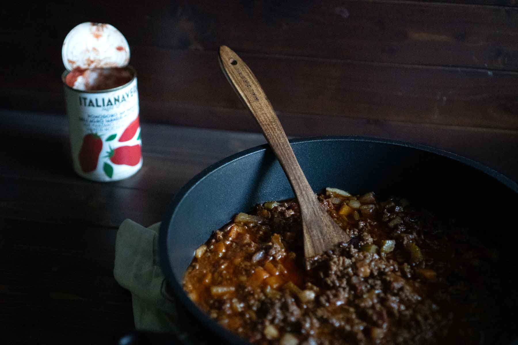 Ragù alla Bolognese in einem Gusseisentopf. Im Hintergrund steht eine geöffnete Dose mit San Marzano Tomaten