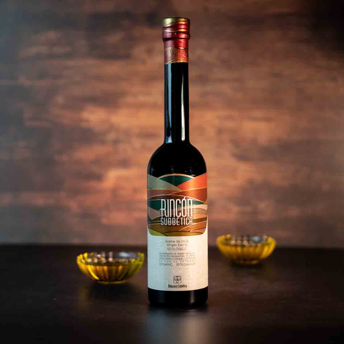 Flasche Rincon Subbetica Olivenöl auf Tisch mit Schalen.