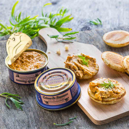 Lachscreme-Dosen auf Holzbrett mit Kräutern und Brot.