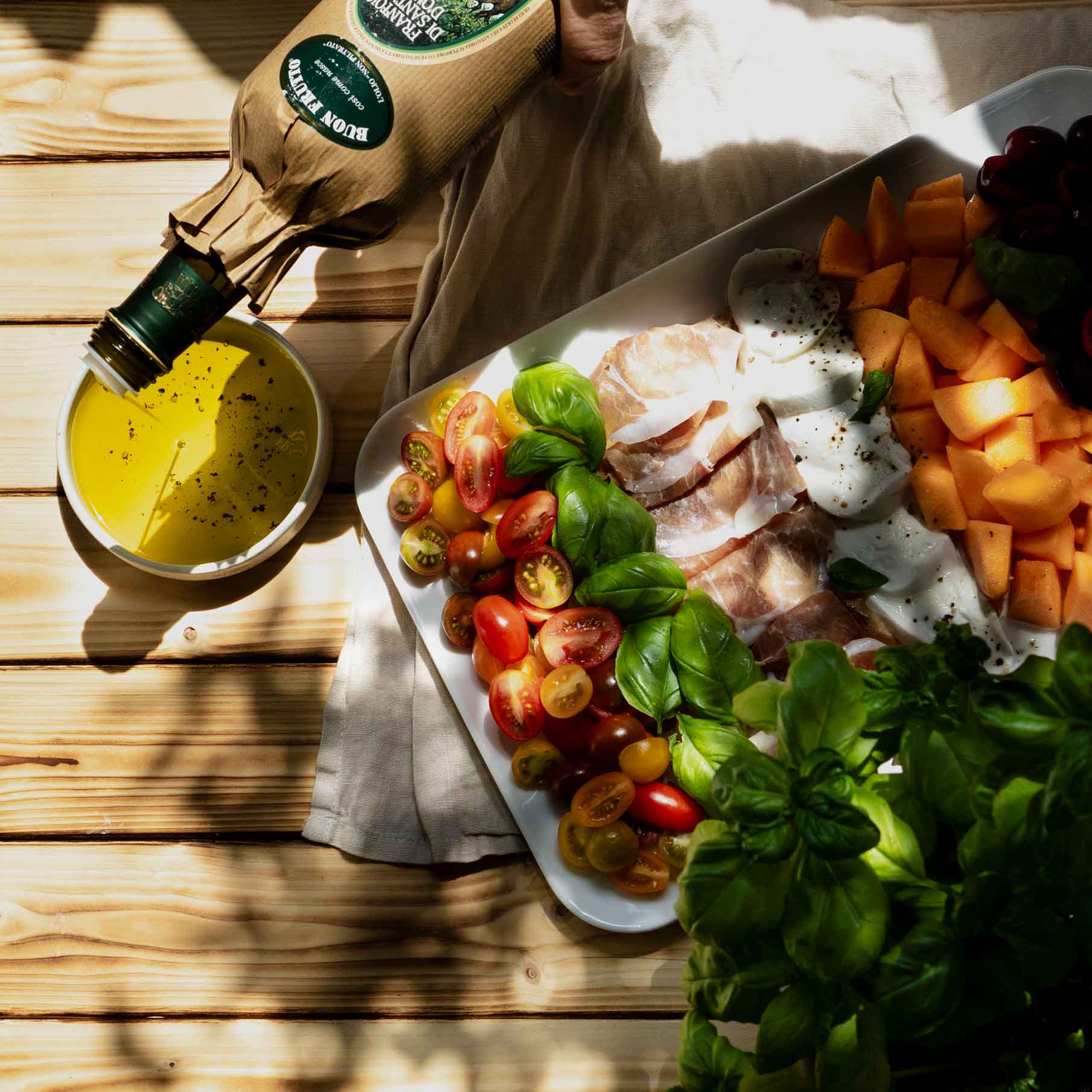 Olivenöl, Tomaten, Basilikum, Melone, Feinkost auf Holzuntergrund.