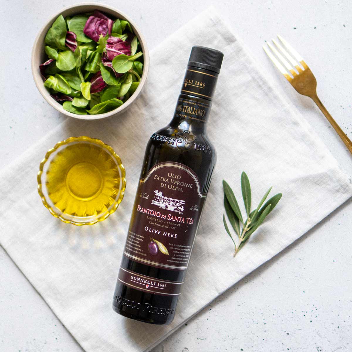 Flasche Olivenöl, Salat, Olivenzweig, Gabel, Schale, Tuch.