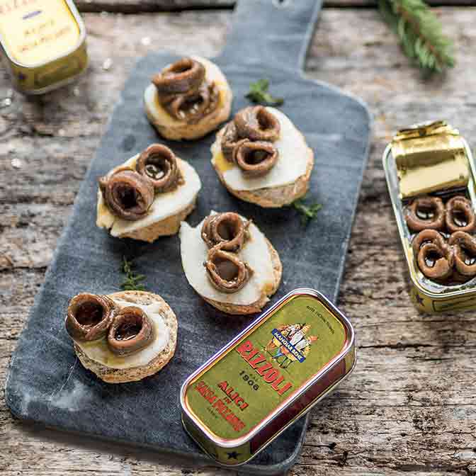 Sardellen auf Brot mit Rizzoli-Dosen auf Holzbrett.