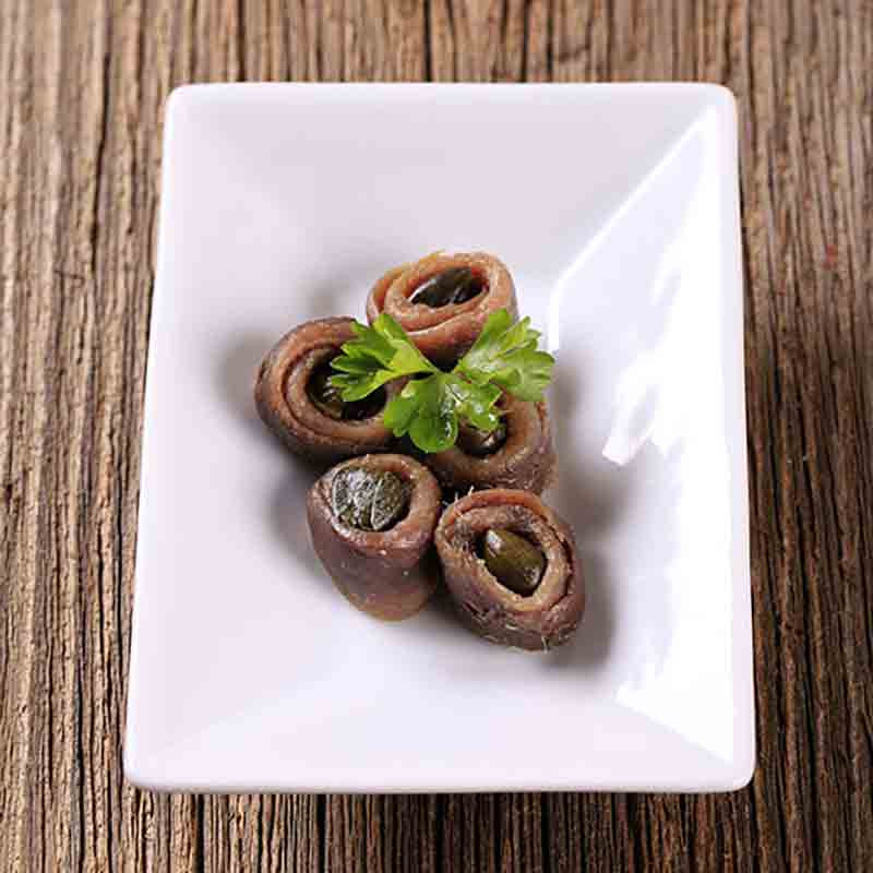 Sardellenröllchen mit Kapern auf weißem Teller, Holztisch.