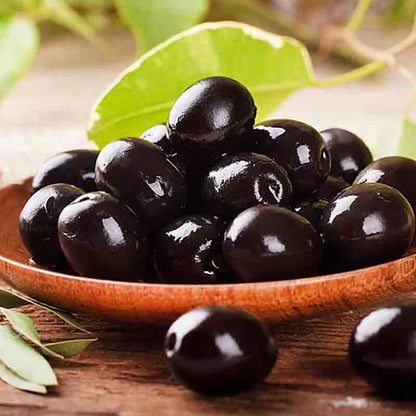 Schwarze Oliven auf Holzschale mit grünen Blättern.