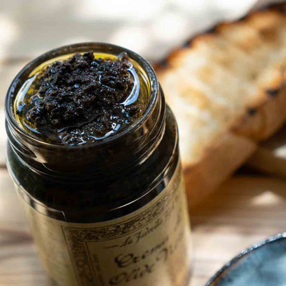 Schwarze Olivencreme im Glas neben geröstetem Brot.
