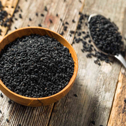 Schwarzkümmelsamen in Holzschale und Löffel auf Holztisch.