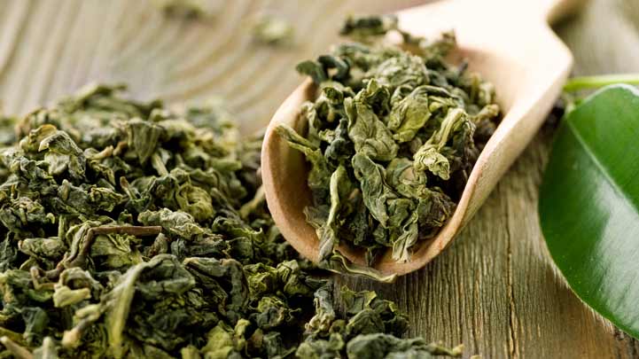 Getrocknete Teeblätter auf Holzlöffel und Tischoberfläche.