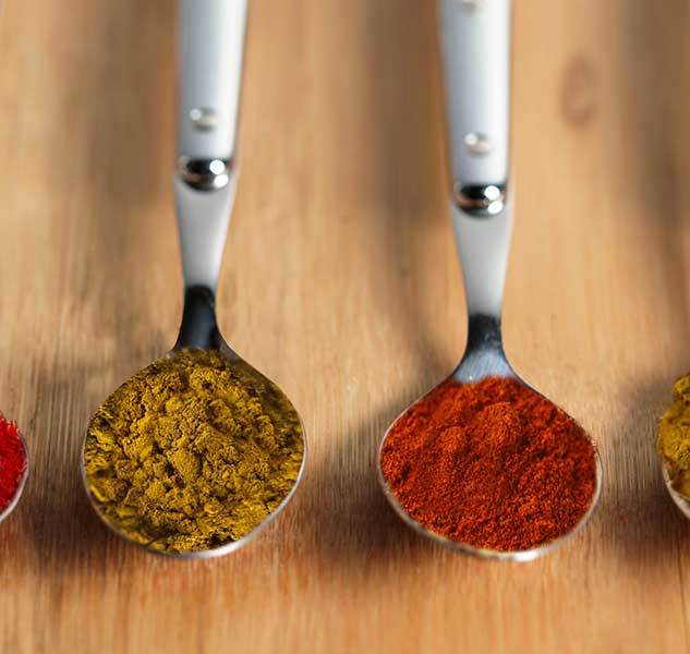 Löffel mit verschiedenen Gewürzen auf Holzoberfläche.