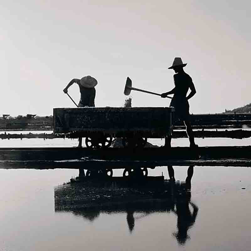 Zwei Salzbauern ernten das Salz von Hand und schippen es in den Salzwagen.