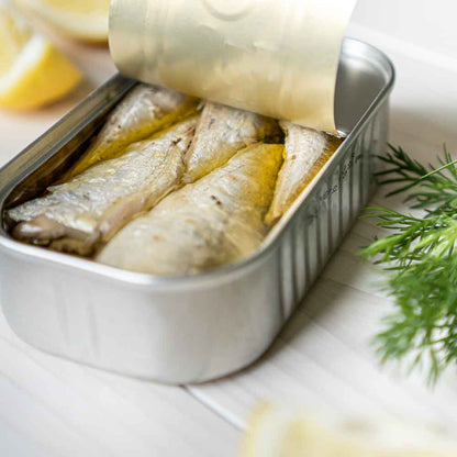 Geöffnete Sardinen-Dose mit Zitrone und Dill auf Tisch.