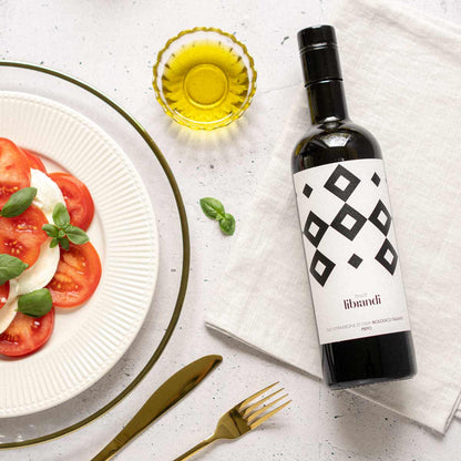 Olivenölflasche Tenute Librandi neben Tomatensalat und Besteck.