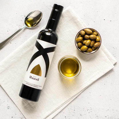 Olivenölflasche Tenute Librandi, Oliven, Löffel, Glas auf Tuch.