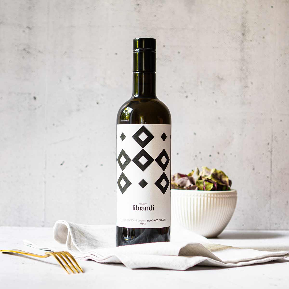 Olivenölflasche von Librandi auf Tisch mit Salatschüssel.
