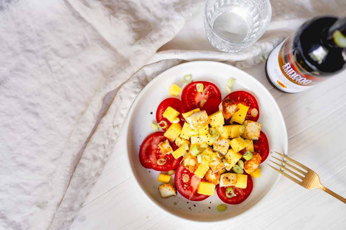 Tomaten-Mango-Salat mit Brot, Glas Wasser, Essigflasche.