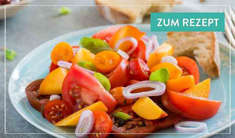 Tomaten-Pfirsich-Salat mit Zwiebeln und Brot auf Teller.