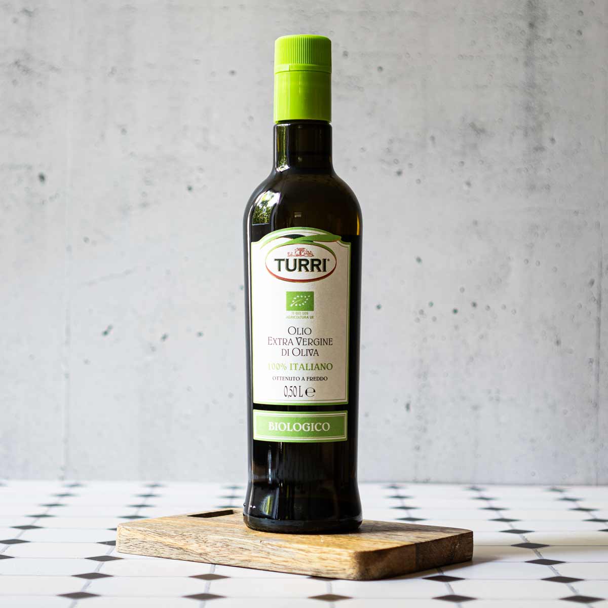 Turri Olivenöl Flasche auf Holzbrett vor grauem Hintergrund.