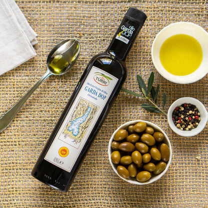 Olivenölflasche Turri, Oliven, Pfeffer, Löffel, Schale auf Tisch.