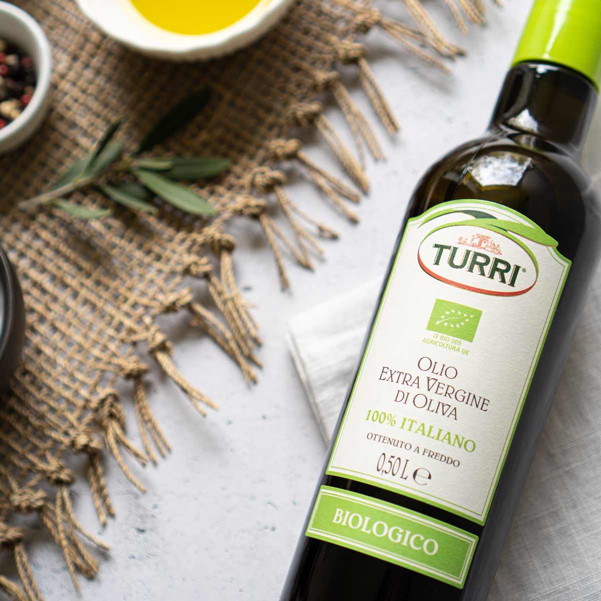 Olivenölflasche Turri, Etikett "Biologico", auf Tisch arrangiert.