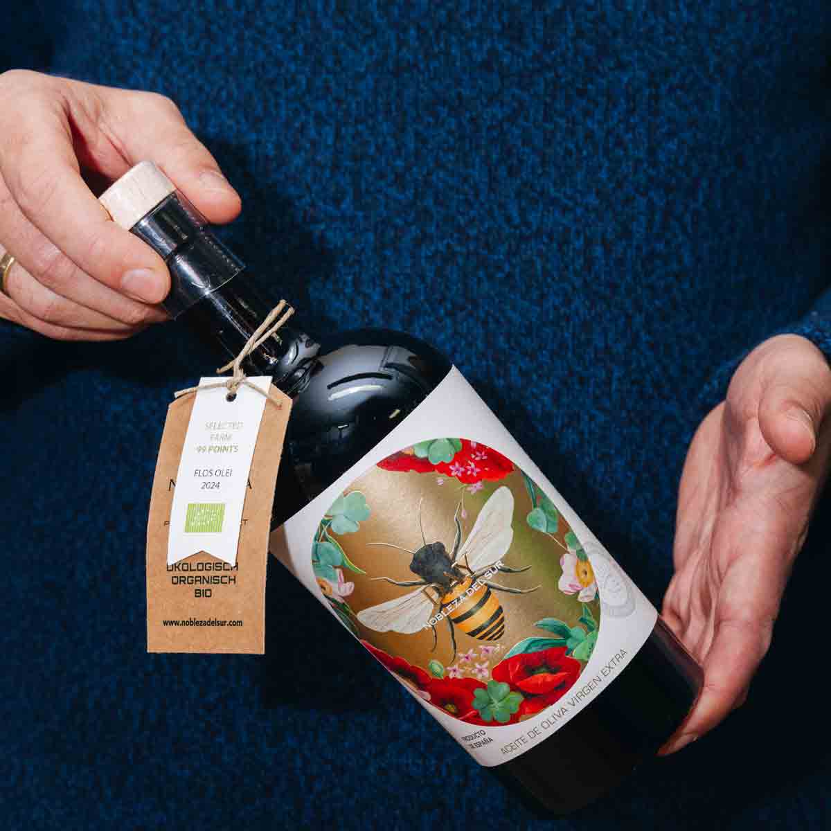 Person hält Weinflasche mit Bienenetikett und Geschenkanhänger.